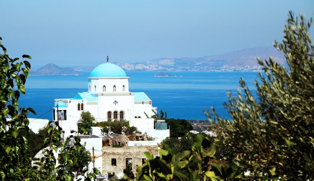 Typische griechische Kirche. Weiß gestrichen mit blauem Kuppeldach. Im Hintergrund das blaue Meer. Sonnenschein. Urlaub